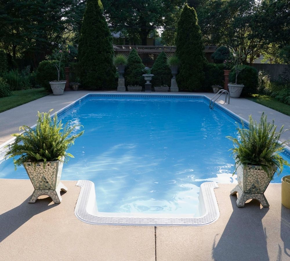 A swimming pool with two potted plants on either side of the steps. | Featured image for Swimming Pool Builders.